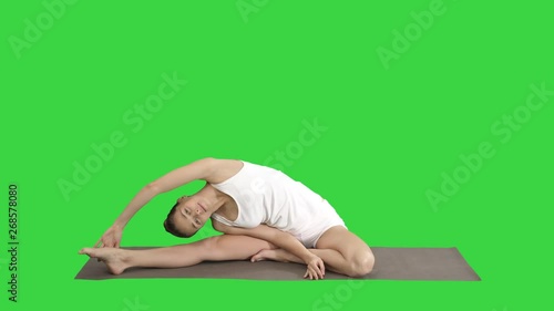 Beautiful young woman wearing white clothing doing yoga exercise Sitting in One-Legged King Pigeon (Single Pigeon) Pose on a Green Screen, Chroma Key. photo