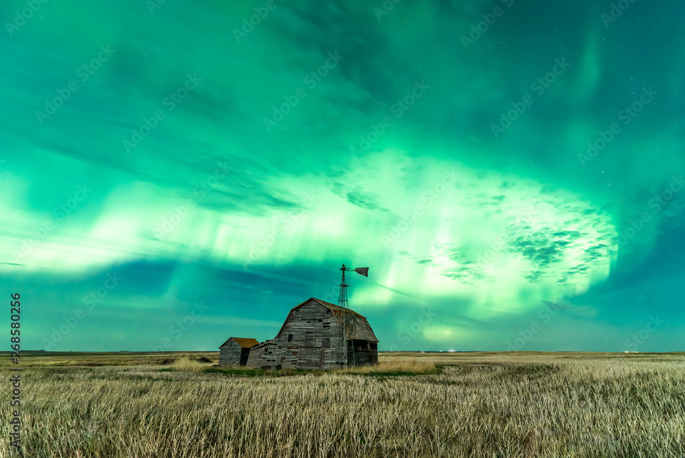 Φωτογραφία Swirl of bright Northern Lights over vintage barn, bins, windmill and stubble in
