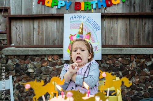 A toddler aged girl scared of the candles on her birthday cake.