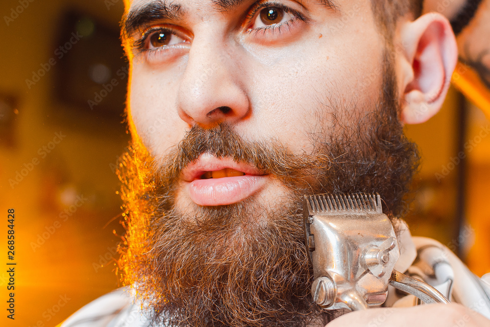 Barber cuts a beard of vintage hair clippers to a young handsome