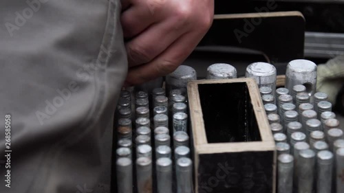 Construction worker's hand collects and puts bunch of cylindric long metallic pins into wooden toolbox with row of round shaped holes outside at daylight time. photo