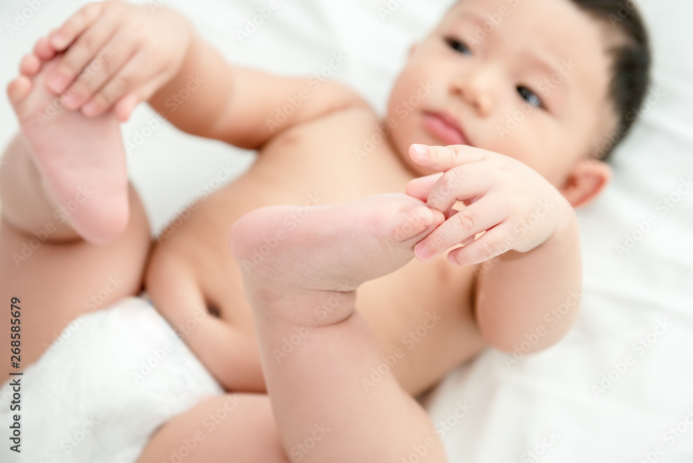 Baby boy lying and relaxing on bed white in the bedroom and holding his legs. Close-up of holding his legs. Baby 6-month skills concept. Baby boy lying and relaxing on bed white in the bedroom and holding his legs. Close-up of holding his legs. Baby 6-month skills concept.