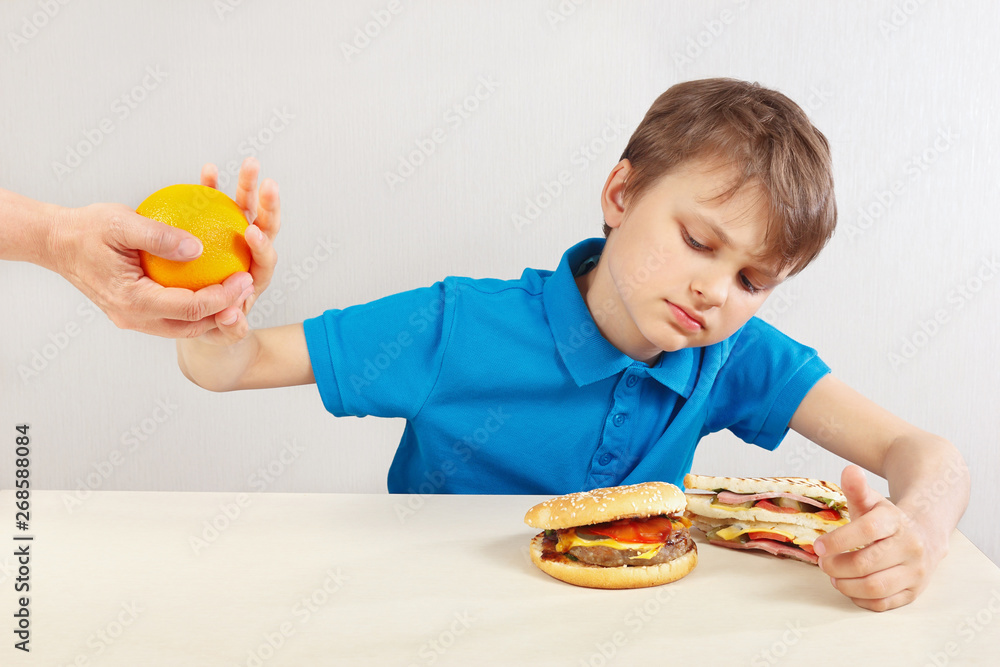 Young boy at the table chooses between fastfood and fruits on a white background Young boy at the table chooses between fastfood and fruits on a white background