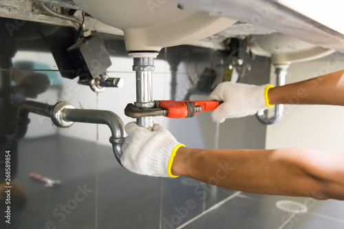 Plumber fixing white sink pipe with adjustable wrench. Fototapeta