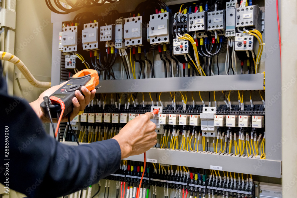 Obraz premium Electrician engineer work tester measuring voltage and current of power electric line in electical cabinet control.