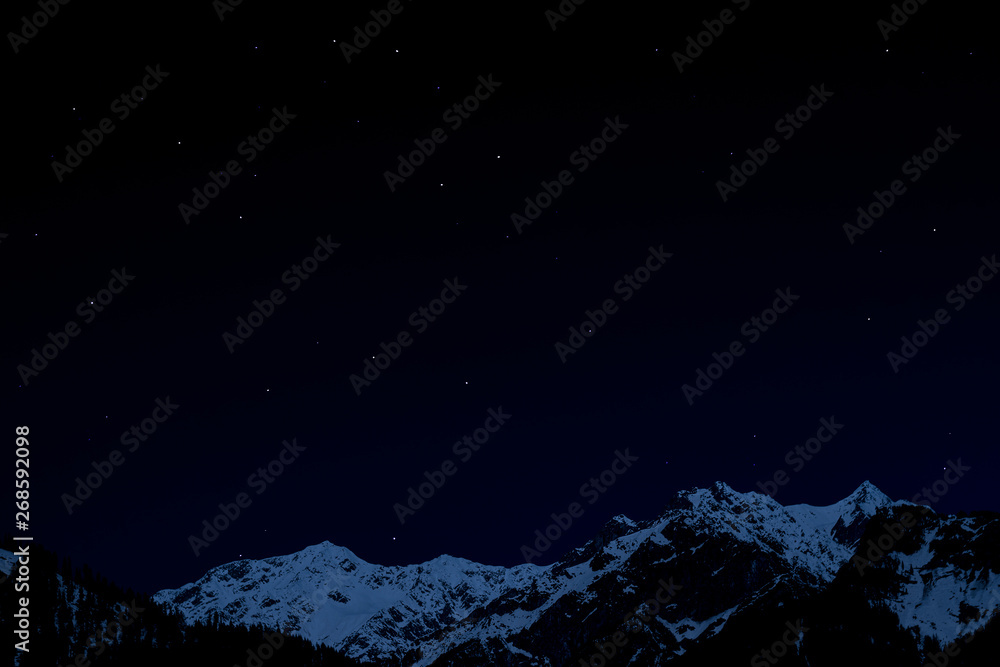 mountain ridge covered with snow-capped peaks winter night with stars and milky way galaxy