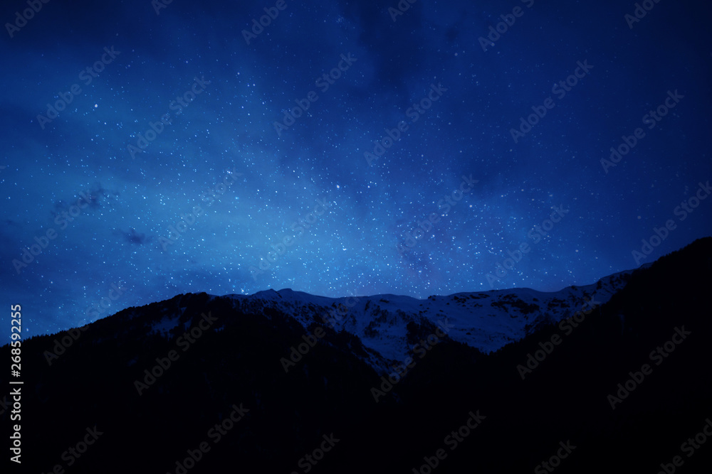 mountain ridge covered with snow-capped peaks winter night with  stars and milky way galaxy