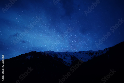 mountain ridge covered with snow-capped peaks winter night with stars and milky way galaxy