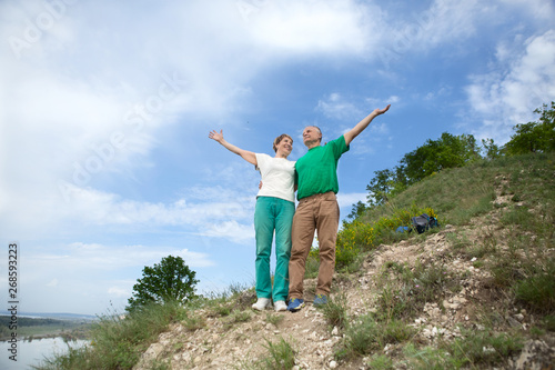 elderly couple on the top of mountain with hands up. Senior couple walking in nature