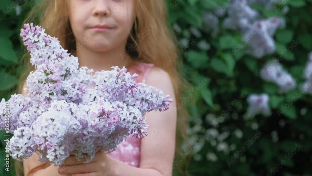 A little girl outdoors in a park or garden holds lilac flowers. Lilac bushes in the background. Summer, park A little girl outdoors in a park or garden holds lilac flowers. Lilac bushes in the background. Summer, park