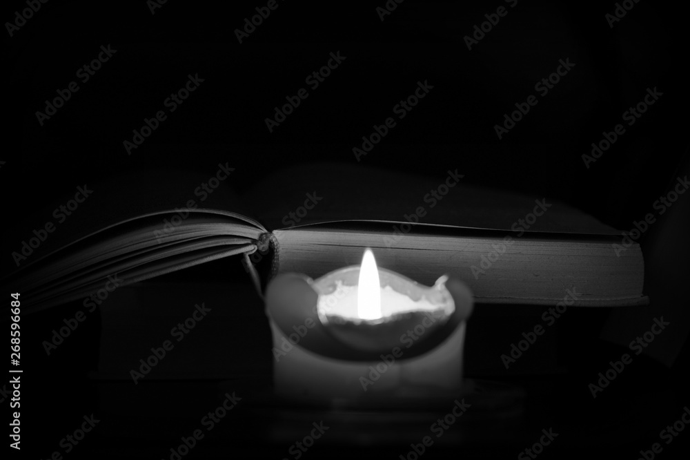 Burning candle and old books in the dark close up. Black and white Burning candle and old books in the dark close up. Black and white