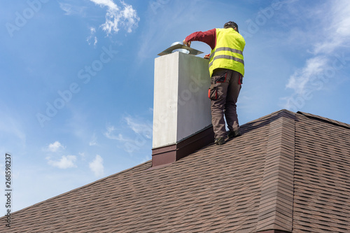 Billede på lærred Man install chimney on roof top of new house under construction