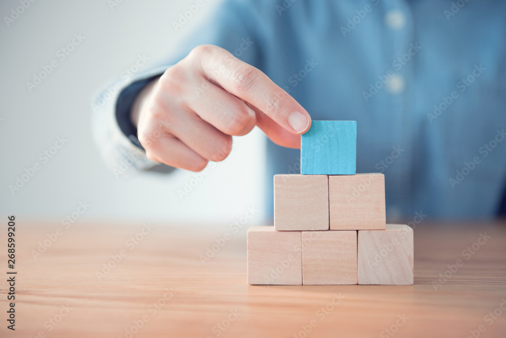 Hand putting blank blue wood cube block on top pyramid, for create icon ...