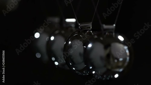 Slow Hit Newtons Balls. Loop. Steel shiny balls suspended on a dark background. They interact with each other, transferring the force of impact. Filmed at a speed of 240fps