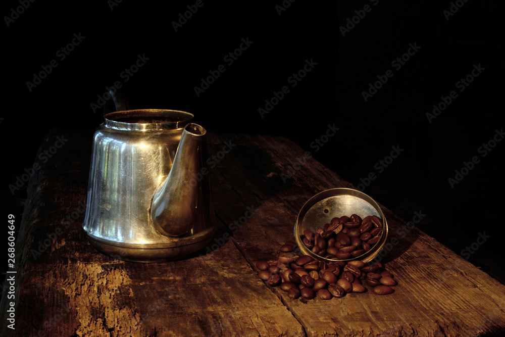 Metal teapot on the old board. There are coffee beans in the lid. Still life. Concept - breakfast