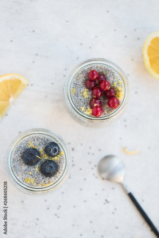 Top view of jars of chia seed pudding made with chia seeds and almond milk and berries, gooseberries, blueberries, lemon zests, shallow depth of field, copy space and light background. Top view of jars of chia seed pudding made with chia seeds and almond milk and berries, gooseberries, blueberries, lemon zests, shallow depth of field, copy space and light background.