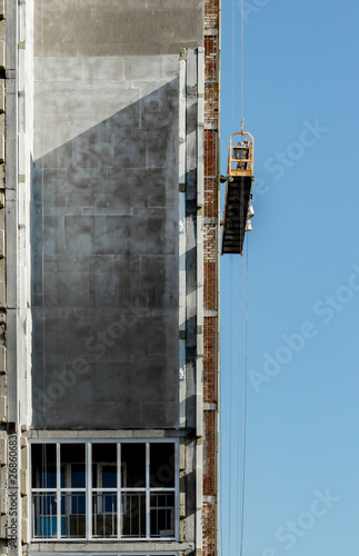 high-rise building under construction against a blue sky, an external elevator moves along the facade