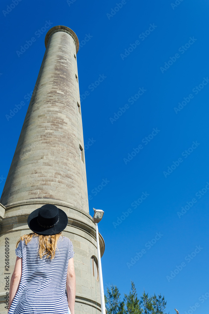 Girl looks at the lighthouse against the blue sky. Bottom view. Travels. Maritime architecture.