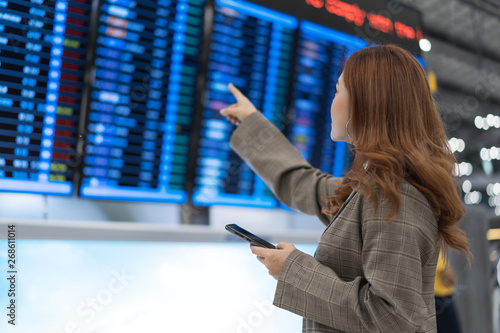 woman using smartphone with flight information board at airport