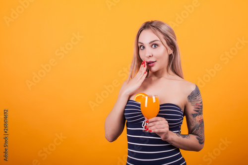 Portrait of pretty girl in sexy swimming suit holding a fresh cocktail over yellow background
