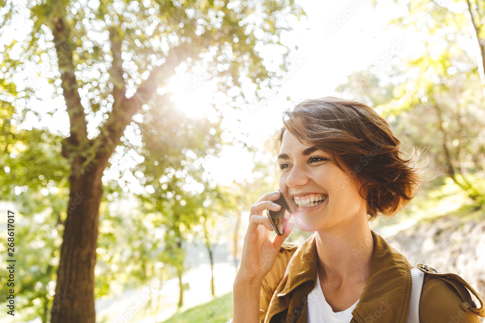 Fototapeta premium Cute young amazing woman walking outdoors in park in beautiful spring day talking by mobile phone.