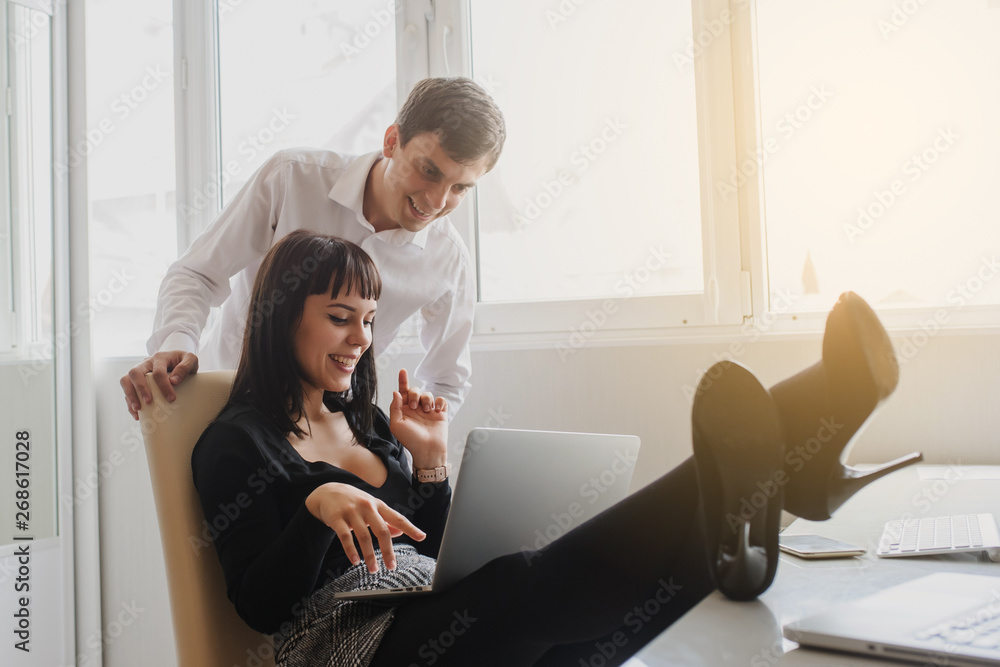 lateral view of a hot brunete talking to a man in office outfit sitting at the table with a computer and a laptop on it lateral view of a hot brunete talking to a man in office outfit sitting at the table with a computer and a laptop on it