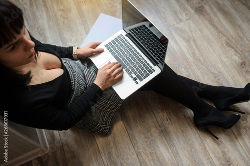 lateral view of a hot brunete in office outfit sitting on the floor and working on computer photo