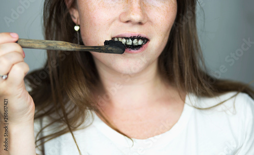 young woman brushing her teeth with a black tooth paste with active charcoal  and black tooth brush on white background for Teeth whitening