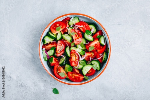 Fresh summer salad bowl with tomatoes, cucumbers, red onions, basil and olive oil dressing.