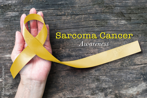 Sarcoma Bone cancer awareness yellow ribbon on human helping hand, aged wood photo