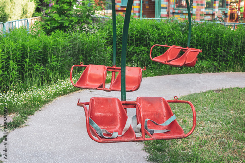 Red seats of children's swings in the old amusement park.
