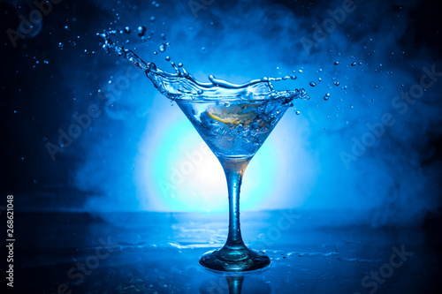 Martini cocktail glass in hand splashing on dark toned smoky background or colorful cocktail in glass with splashes and olives. Party club entertainment. Mixed light. Selective focus