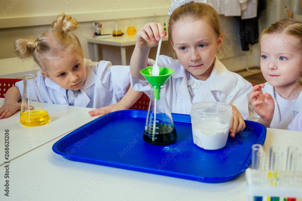 group of school girl kids with teacher in school laboratory making experiment observing the chemical reaction with the dye with vinegar and soda volcano wearing white gown uniform glass