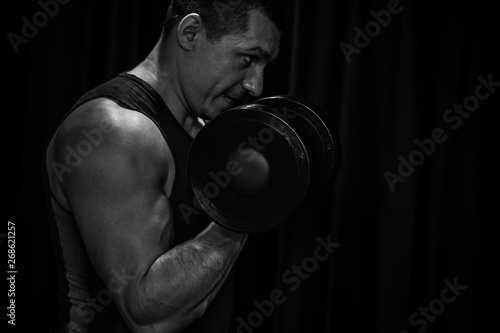 athlete trains biceps hands with dumbbells in the center of workouts on a black background. training tools in the gym close-up