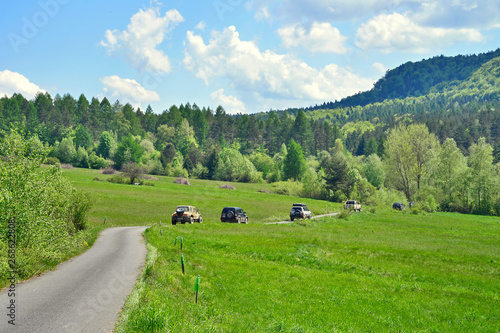 Off-road cars driving along winding road among the green hills in spring sunny day, Low Beskids (Beskid Niski), Poland