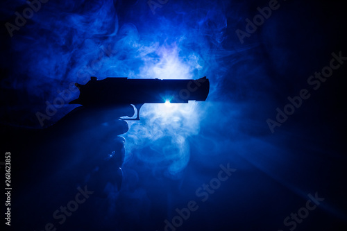 Obraz na plátně Male hand holding gun on black background with smoke toned back lights