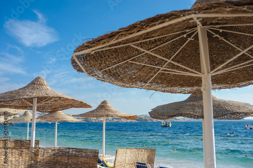 Fototapeta Naklejka Na Ścianę i Meble -  Thatched beach umbrellas and loungers on a beach at an idyllic tropical resort for a summer vacation