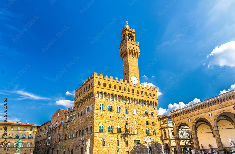 Palazzo Vecchio palace with bell tower with clock and Loggia dei Lanzi on Piazza della Signoria square in historical centre of Florence city, blue sky white clouds, Tuscany, Italy