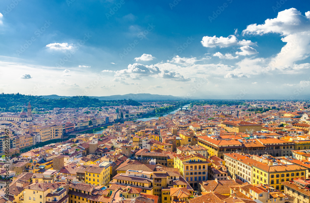 Top aerial panoramic view of Florence city historical centre, bridges over Arno river, buildings houses with orange red tiled roofs, blue sky white clouds background, Tuscany, Italy