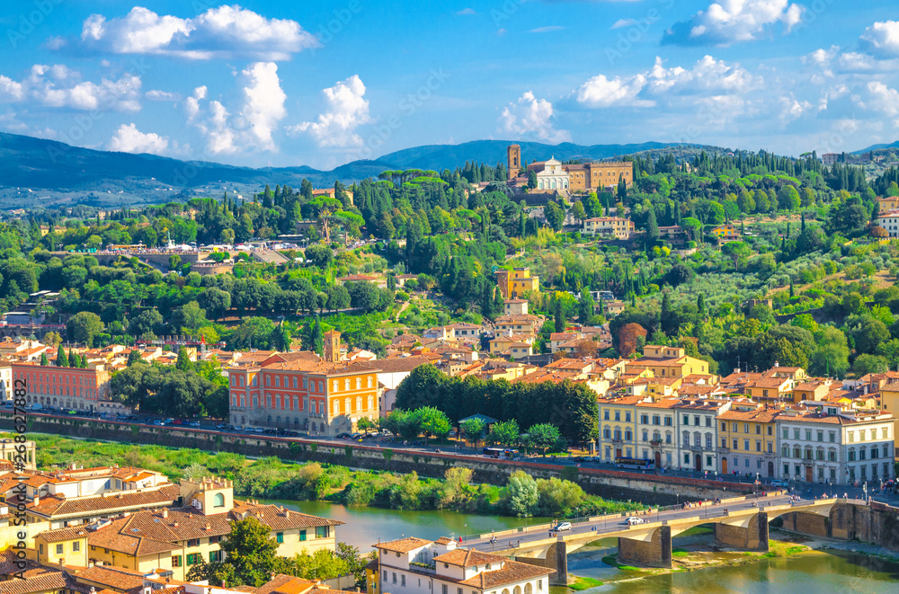Top aerial panoramic view of green hills with Abbazia di San Miniato al Monte, bridges over Arno river, blue sky white clouds background, Florence city, Tuscany, Italy