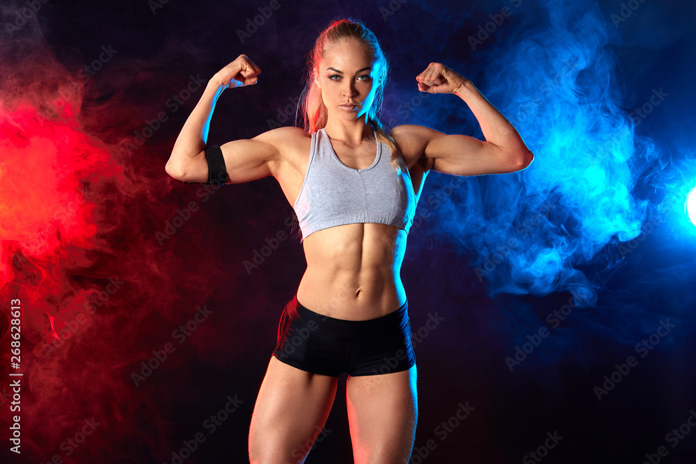 Obraz premium attractive female athlete is good at sport, woman leads healthy lifestyle. isolated black nbackground with redand blue smoke