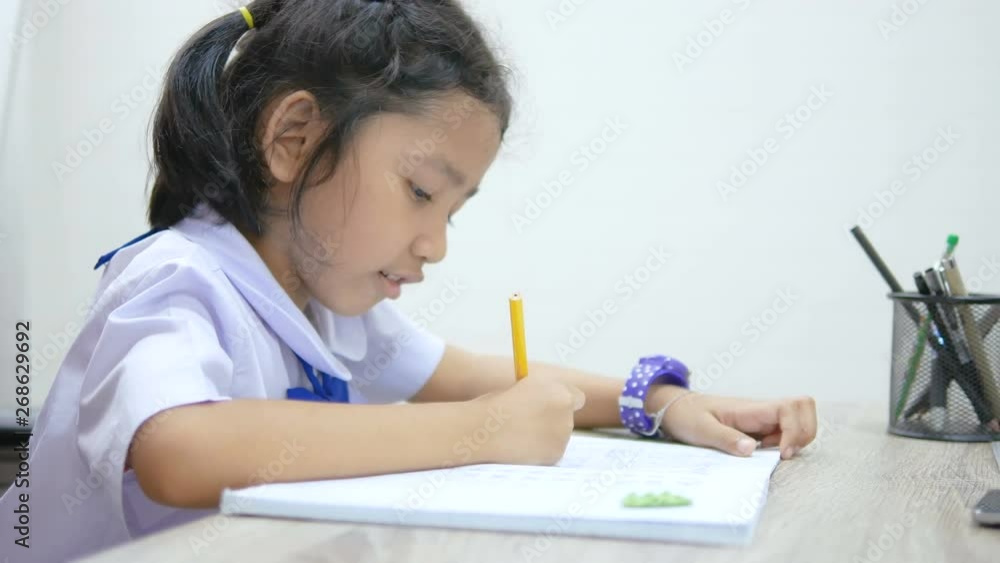 Asian little girl in Thai student uniform doing homework on wooden table select focus shallow depth of field Asian little girl in Thai student uniform doing homework on wooden table select focus shallow depth of field