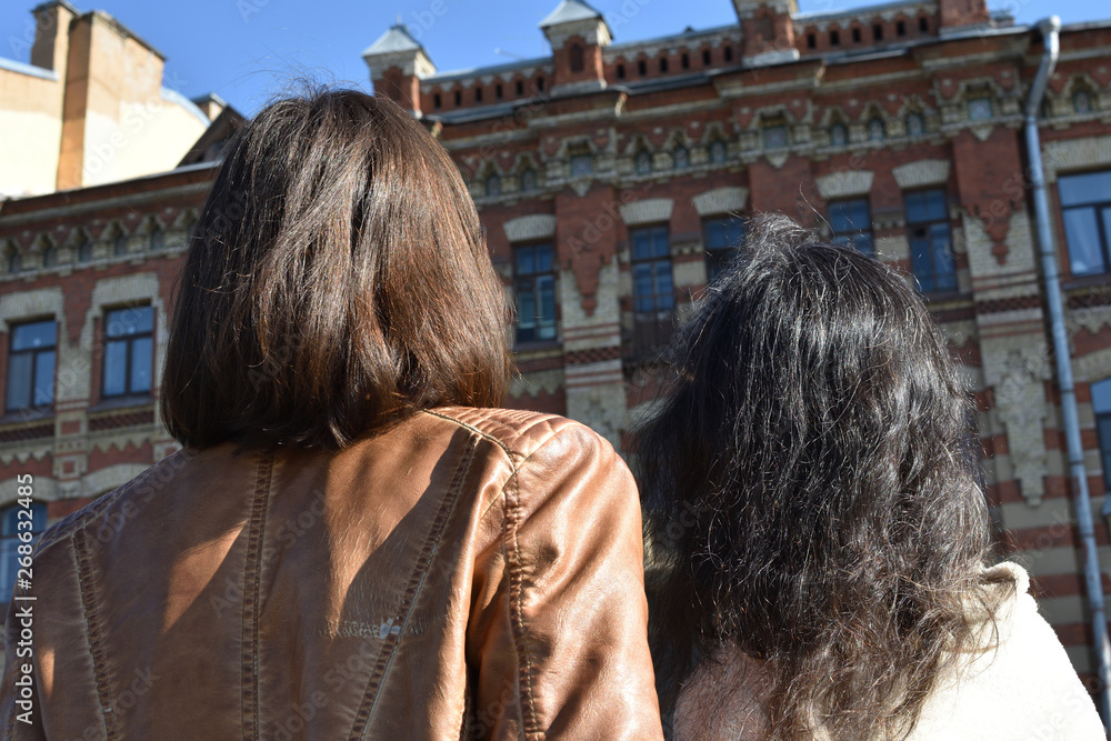 Fototapeta premium young ladies tourists in Saint Petersburg Russia stand on a bridge at a yellow buildings square and watch architectural details of a building