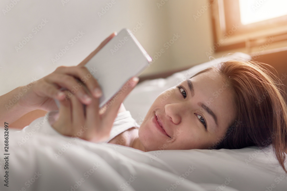 Young asian woman playing with her smathphone on white pillow on bed in bedroom on morning time after wake up, Selective focus. Young asian woman playing with her smathphone on white pillow on bed in bedroom on morning time after wake up, Selective focus.