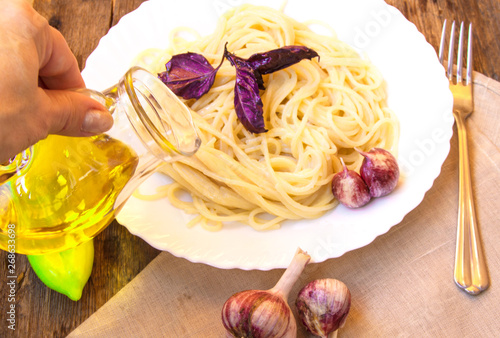 Italian cuisine, spaghetti with Basil and garlic, a woman's hand holding a glass jug of olive oil photo