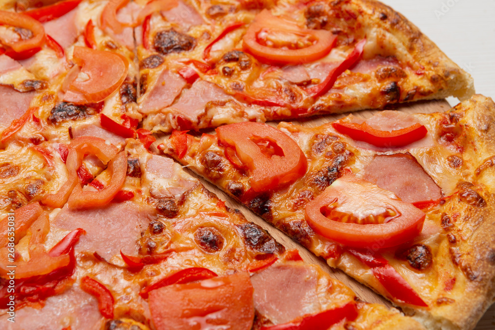 Italian pizza with slices of prosciutto meat and tomatoes, pizza cut, close-up Italian pizza with slices of prosciutto meat and tomatoes, pizza cut, close-up