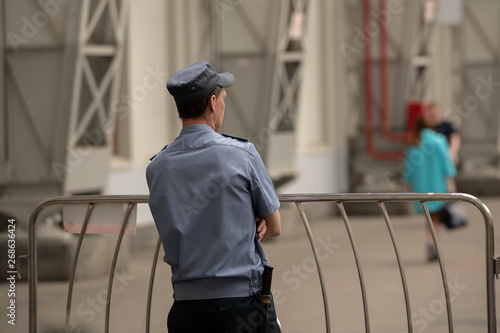 Security officer in a light blue uniform stands near a metal fence