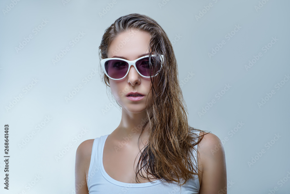 Close up portrait of beautiful young woman in fashionable white sunglasses and white shirt is posing stylishly isolated on gray background in a studio Close up portrait of beautiful young woman in fashionable white sunglasses and white shirt is posing stylishly isolated on gray background in a studio