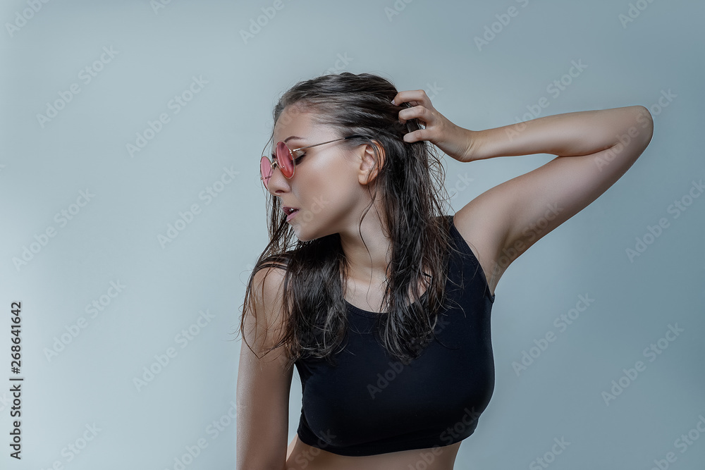 Portrait of beautiful young woman in fashionable round pink sunglasses and black shirt with wet hair is posing stylishly in profile isolated on gray background close up Portrait of beautiful young woman in fashionable round pink sunglasses and black shirt with wet hair is posing stylishly in profile isolated on gray background close up