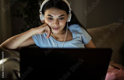 Single woman watching online tv in the night sitting on a couch in the living room at home photo